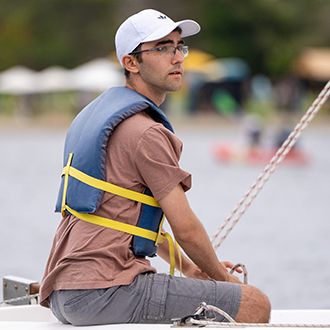 A man saling in a boat on shoreline lake.