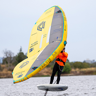 A man using a wingfoil on shoreline lake.