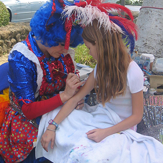 A young girl getting her painted by a clown.