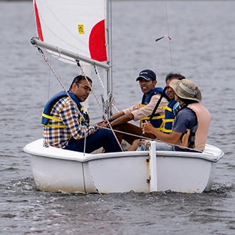 men in a sailbaot on shoreline lake receiving racing instruction.