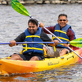 two men rowing a kayak on shoreline lake.