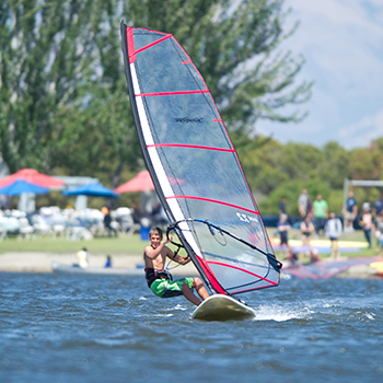 A boy moving fast on a windsurf board in the middle of the lake.